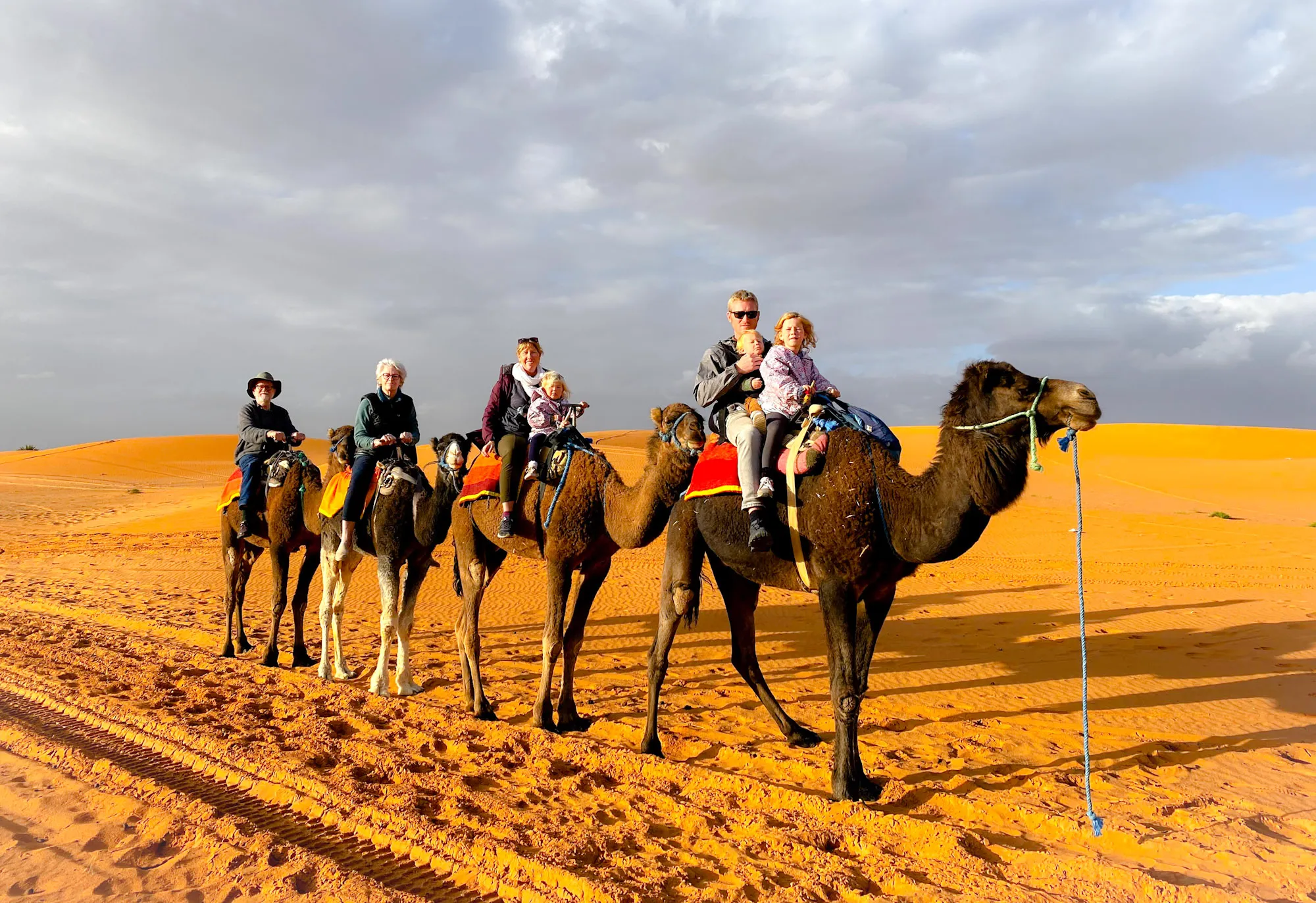 Family riding camels in the Morocco desert at sunset